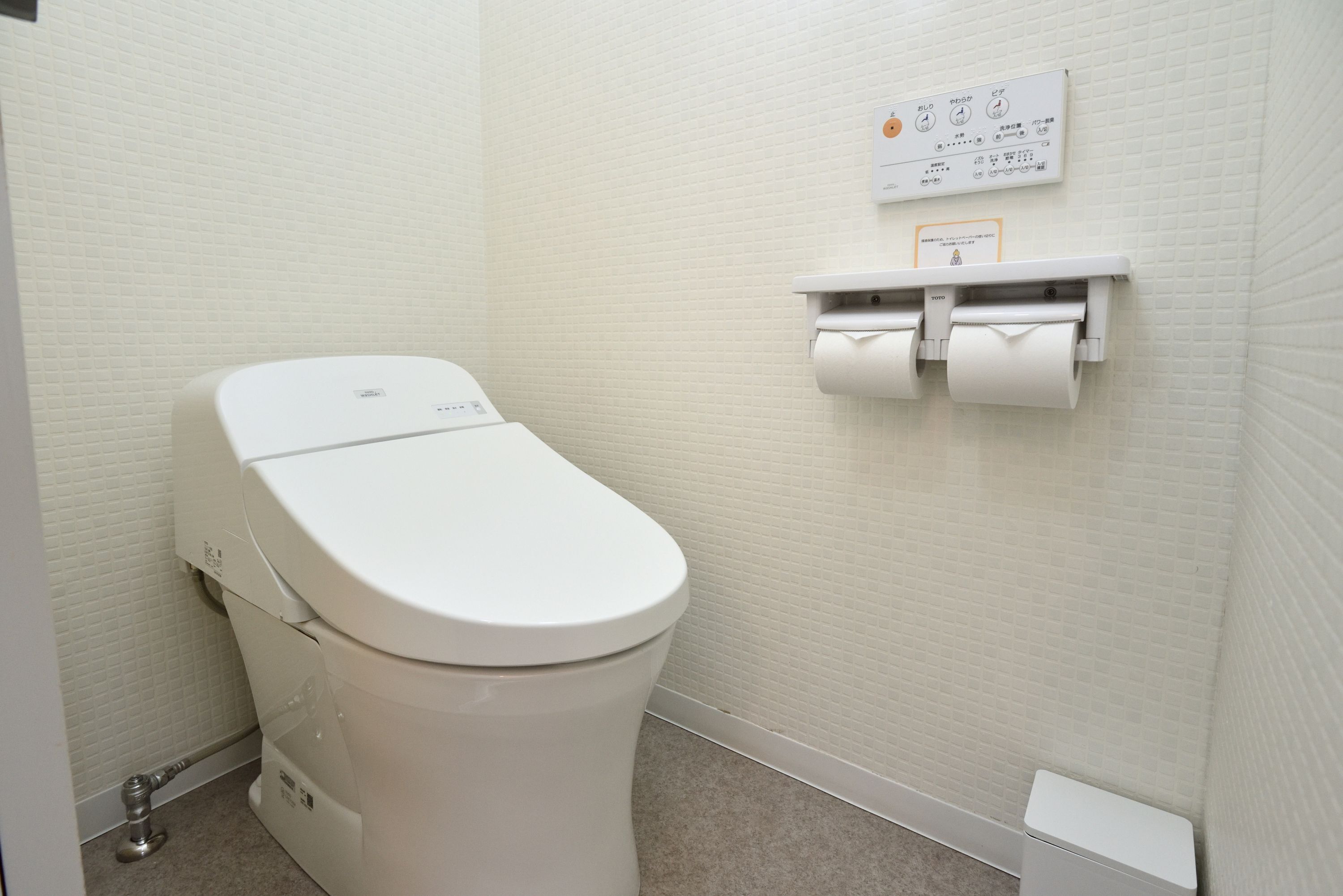 A white toilet with a flush handle, a paper towel dispenser, and a toilet paper roll.