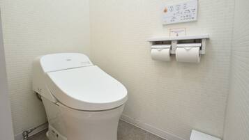A white toilet with a flush handle, a paper towel dispenser, and a toilet paper roll.