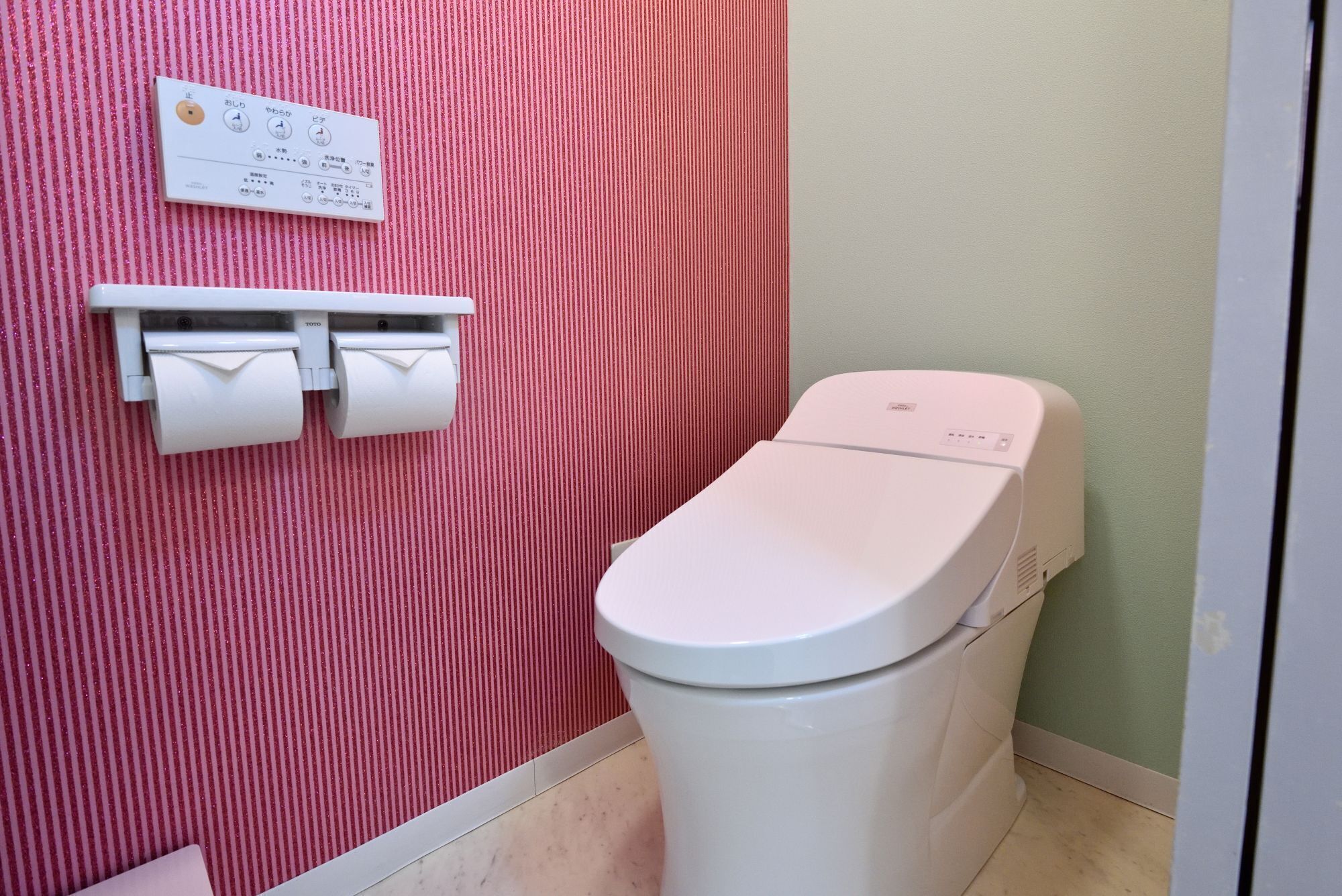 A bathroom with a toilet, a wall-mounted flush control panel, and a toilet paper holder.