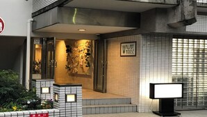 Entrada de um edifício com fachada em azulejos, um letreiro com a inscrição 'Wallaby House' e uma pequena área de estar ao ar livre com degraus.