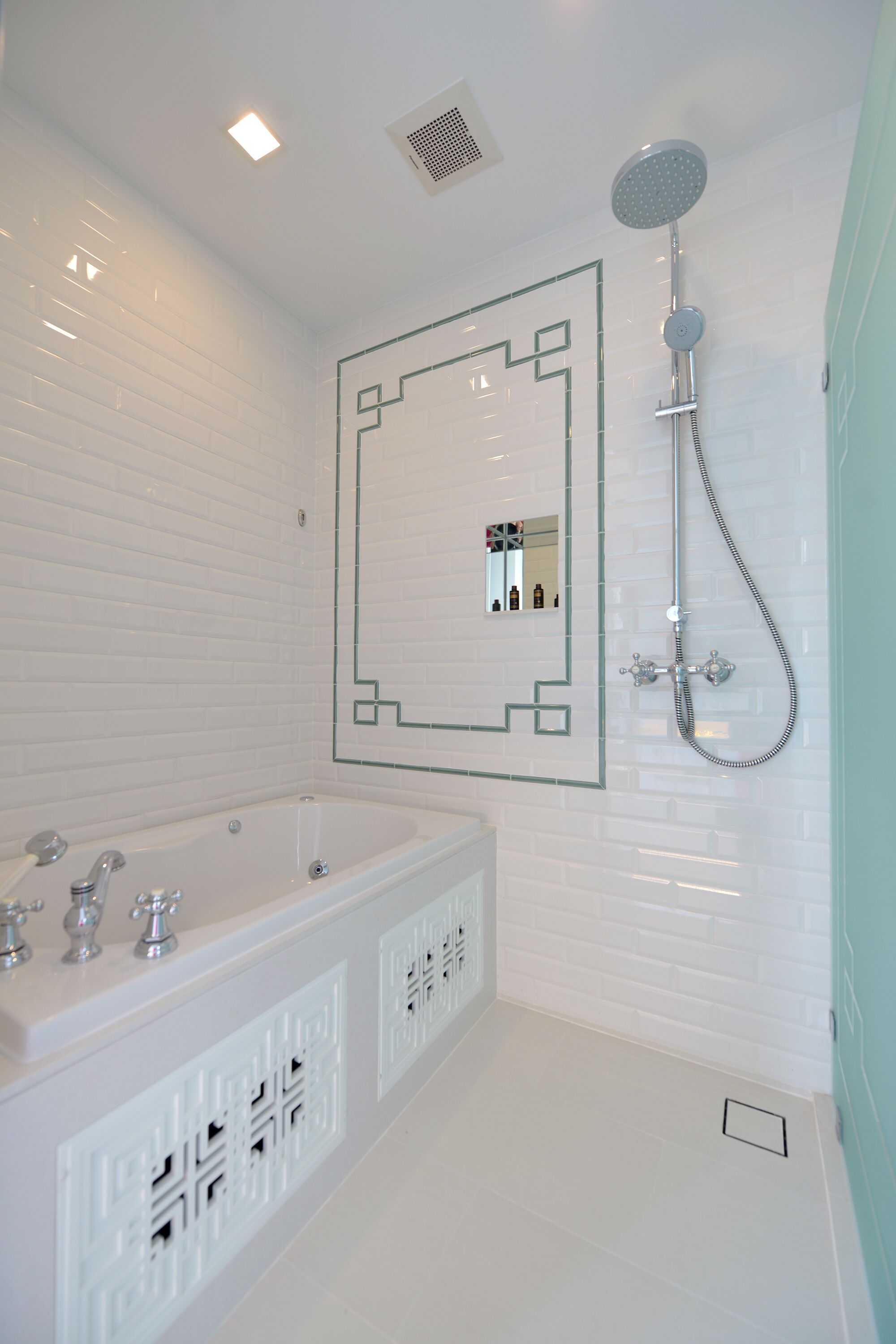 Un baño moderno con una bañera grande, un cabezal de ducha y un espejo con diseño geométrico en la pared.