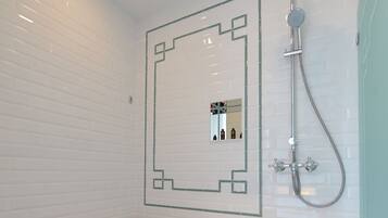 Un baño moderno con una bañera grande, un cabezal de ducha y un espejo con diseño geométrico en la pared.