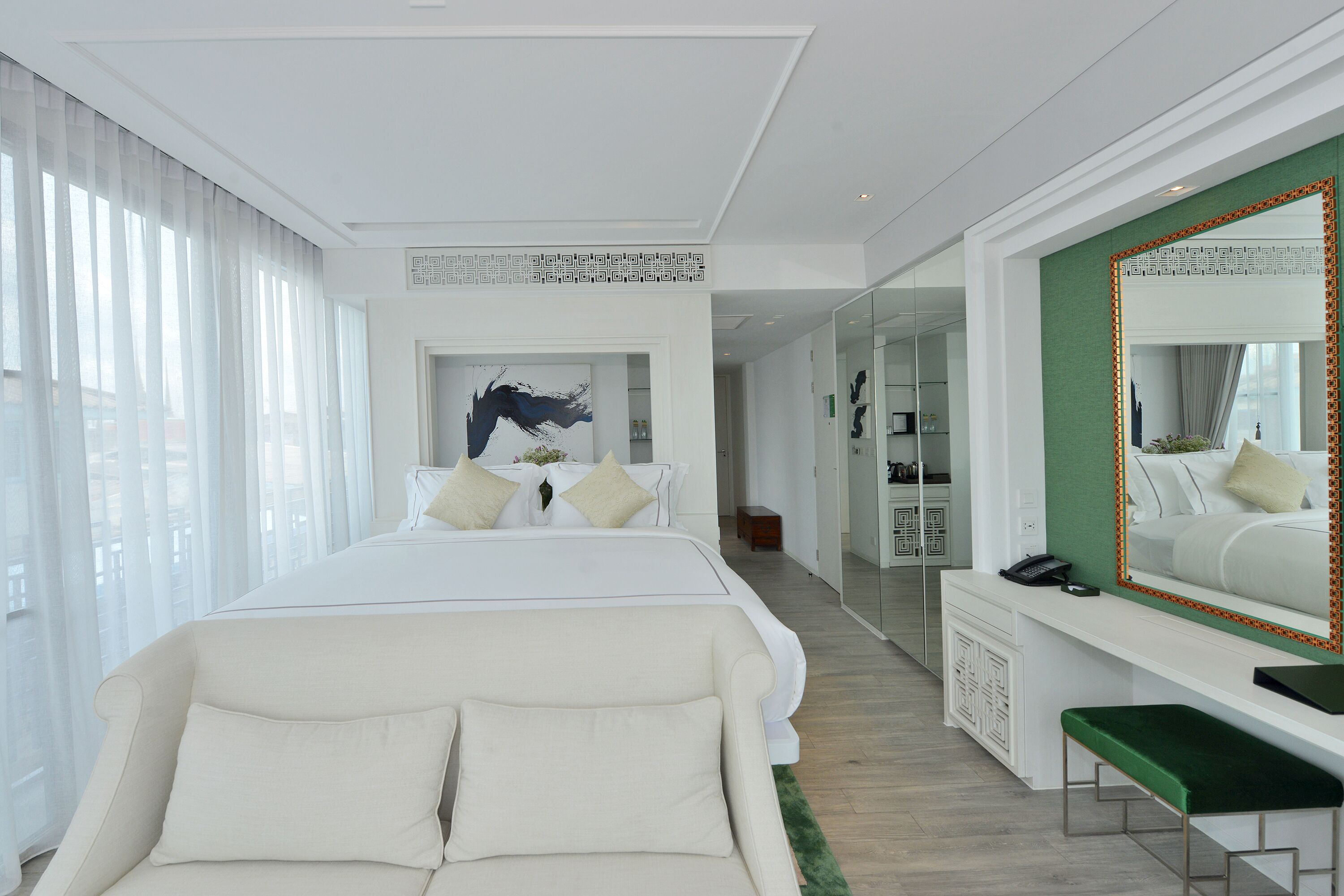 A modern hotel room with a large bed, a green accent wall, a large mirror, and a desk with a telephone.