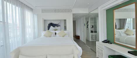 A modern hotel room with a large bed, a green accent wall, a large mirror, and a desk with a telephone.
