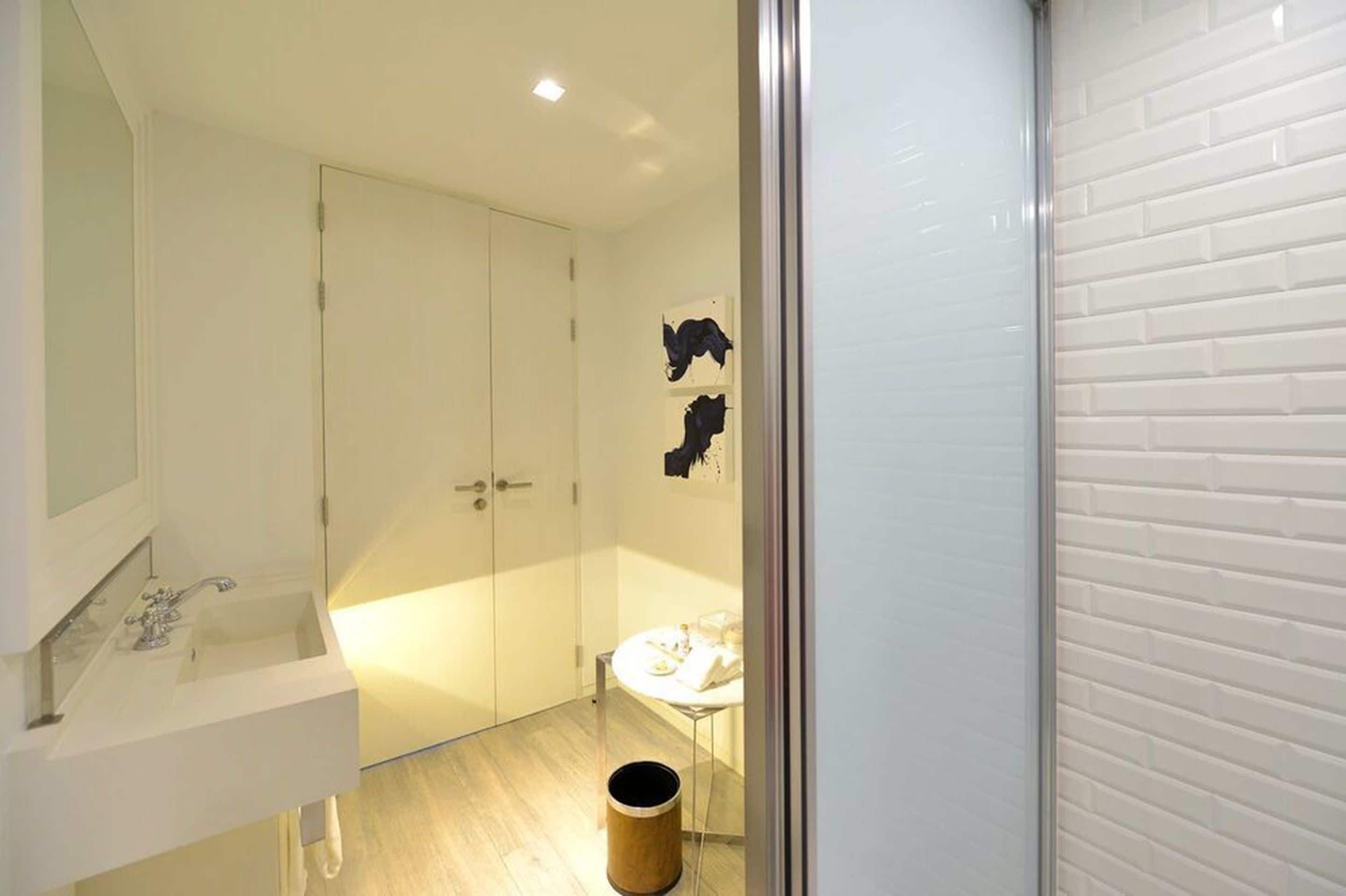 A bathroom with a white sink, mirror, and toilet. There is a trash can and a towel rack.