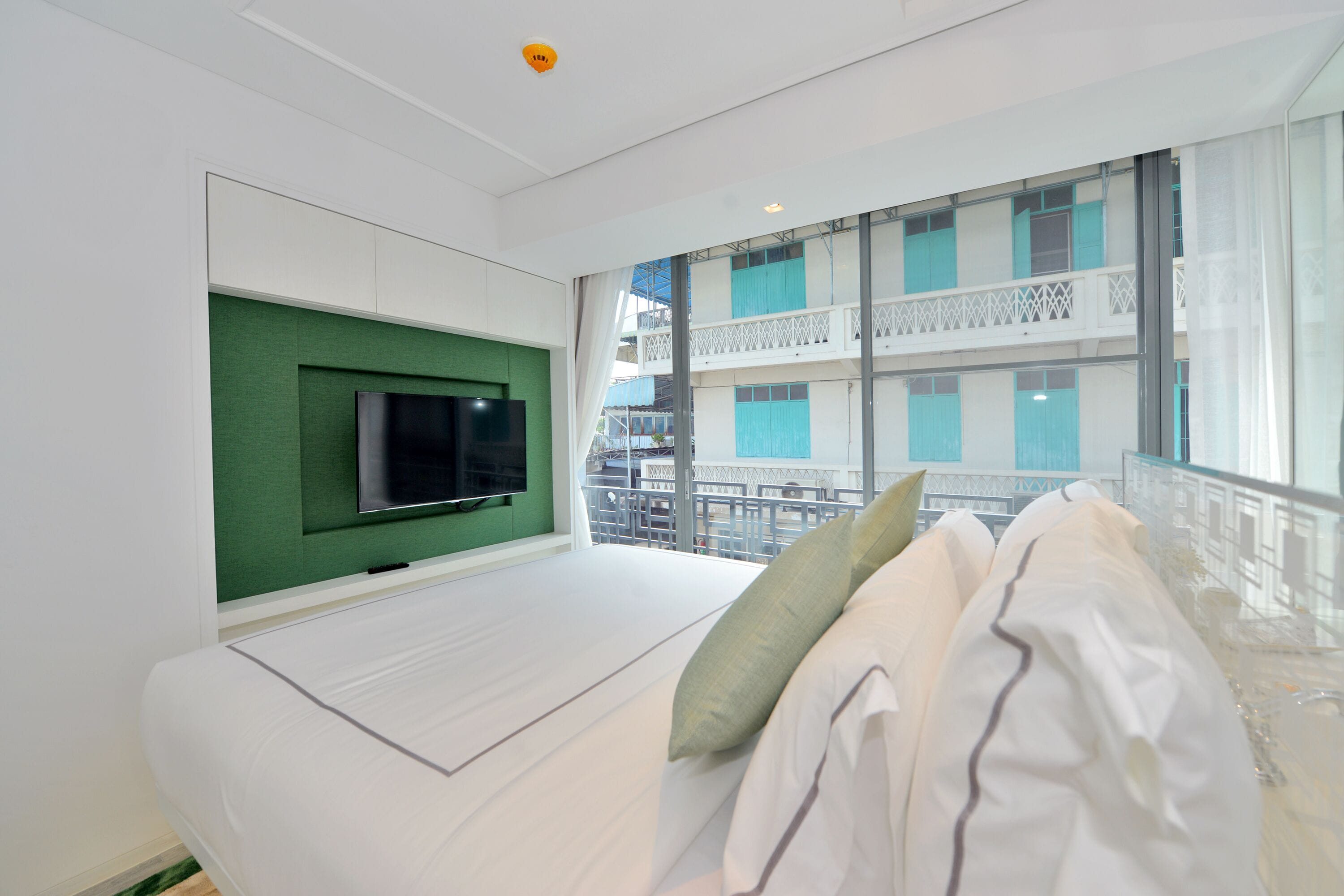 Una habitación de hotel moderna con una cama grande, un televisor montado y un balcón con vista a la ciudad.
