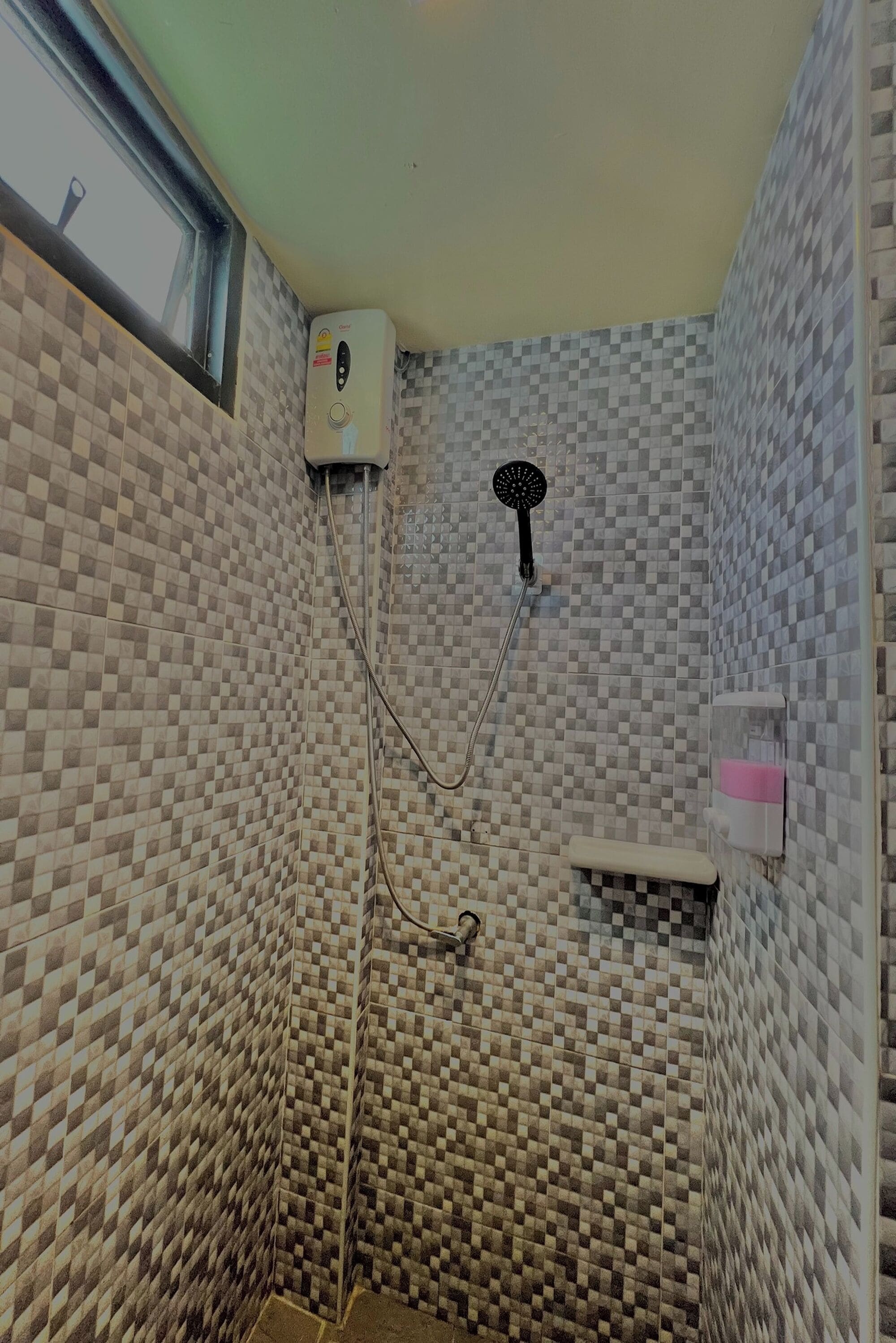 Een badkamer met een wand betegeld met zwart-wit schaakbordmotief, een handdouche, een handdoekdispenser en een raam.