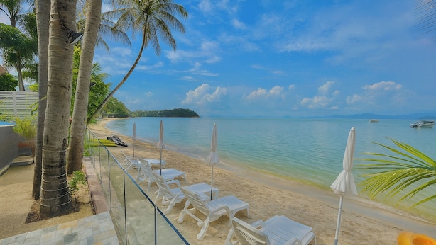 A beach with white lounge chairs and umbrellas, a clear view of the sea, and a distant island. - The Shore Samui (Koh Samui)