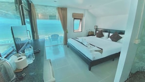 A hotel room with a bed, a desk with a chair, a window with a view, and a small table with toiletries. - The Shore Samui (Koh Samui)