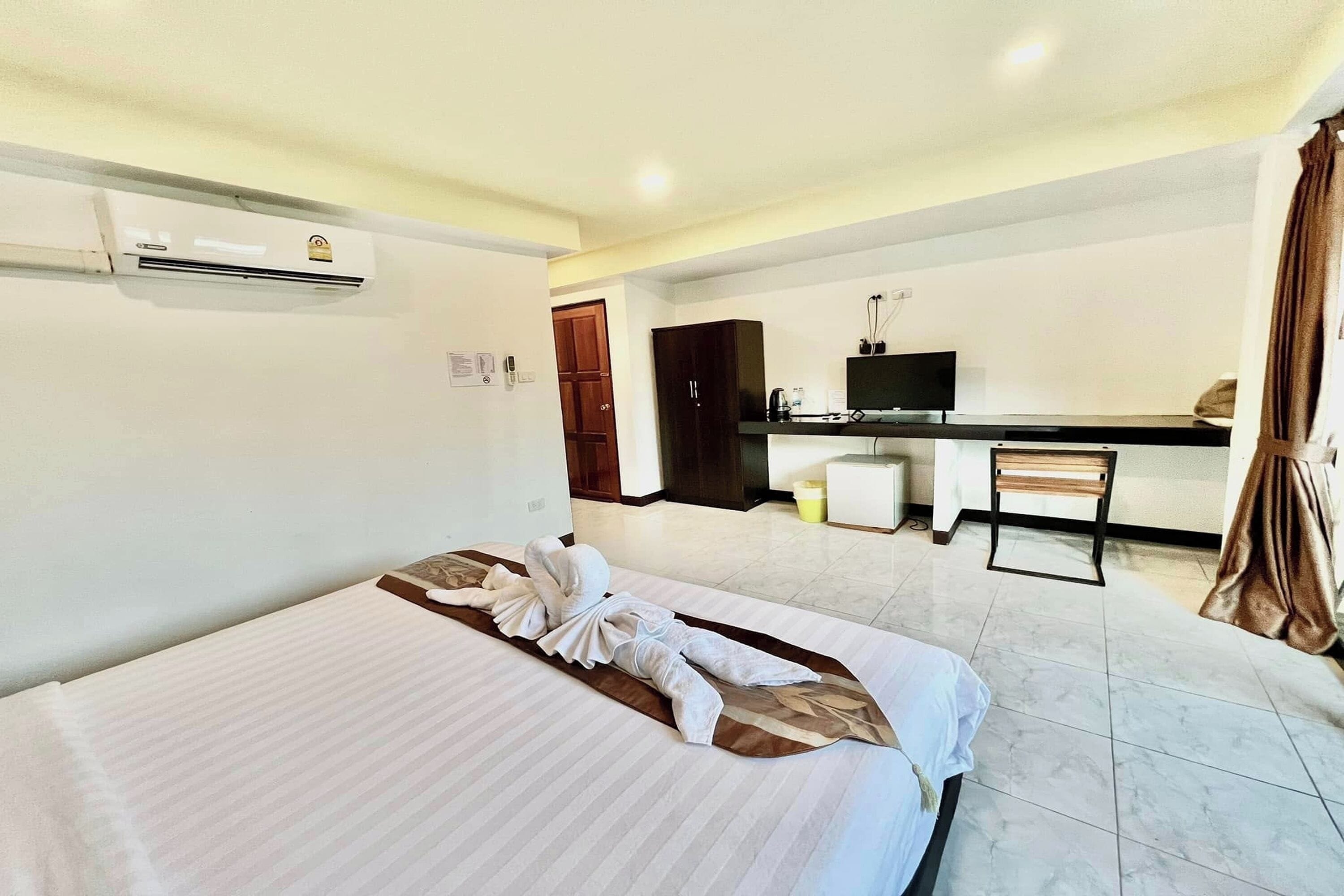 A hotel room with a bed, a desk, a television, and an air conditioning unit.