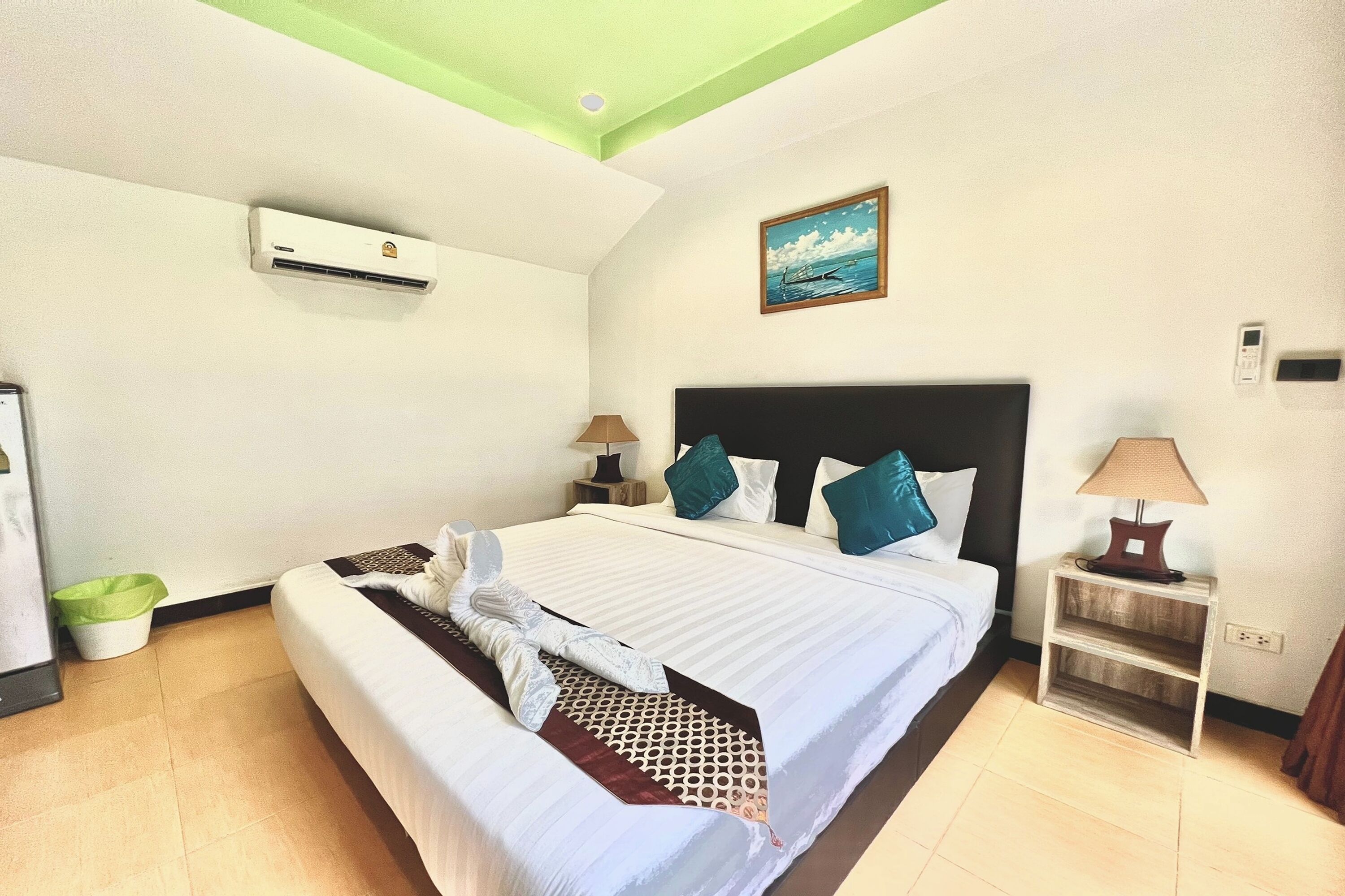 Une chambre d’hôtel avec un lit, une table de chevet, une lampe, un climatiseur, un tableau et un plafond vert.