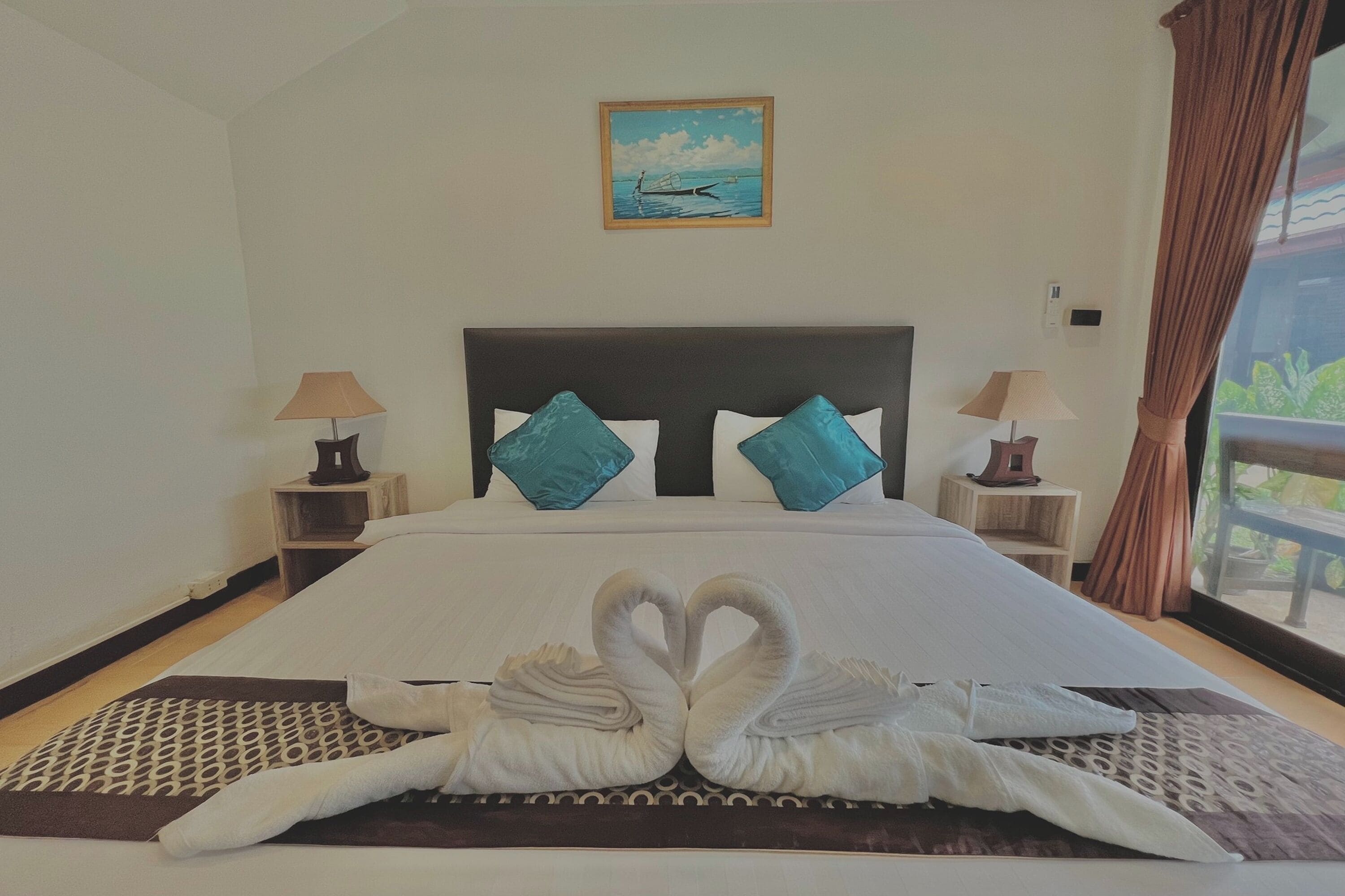 Une chambre d’hôtel avec un grand lit, deux tables de chevet, un tableau au mur et une vue par la fenêtre.