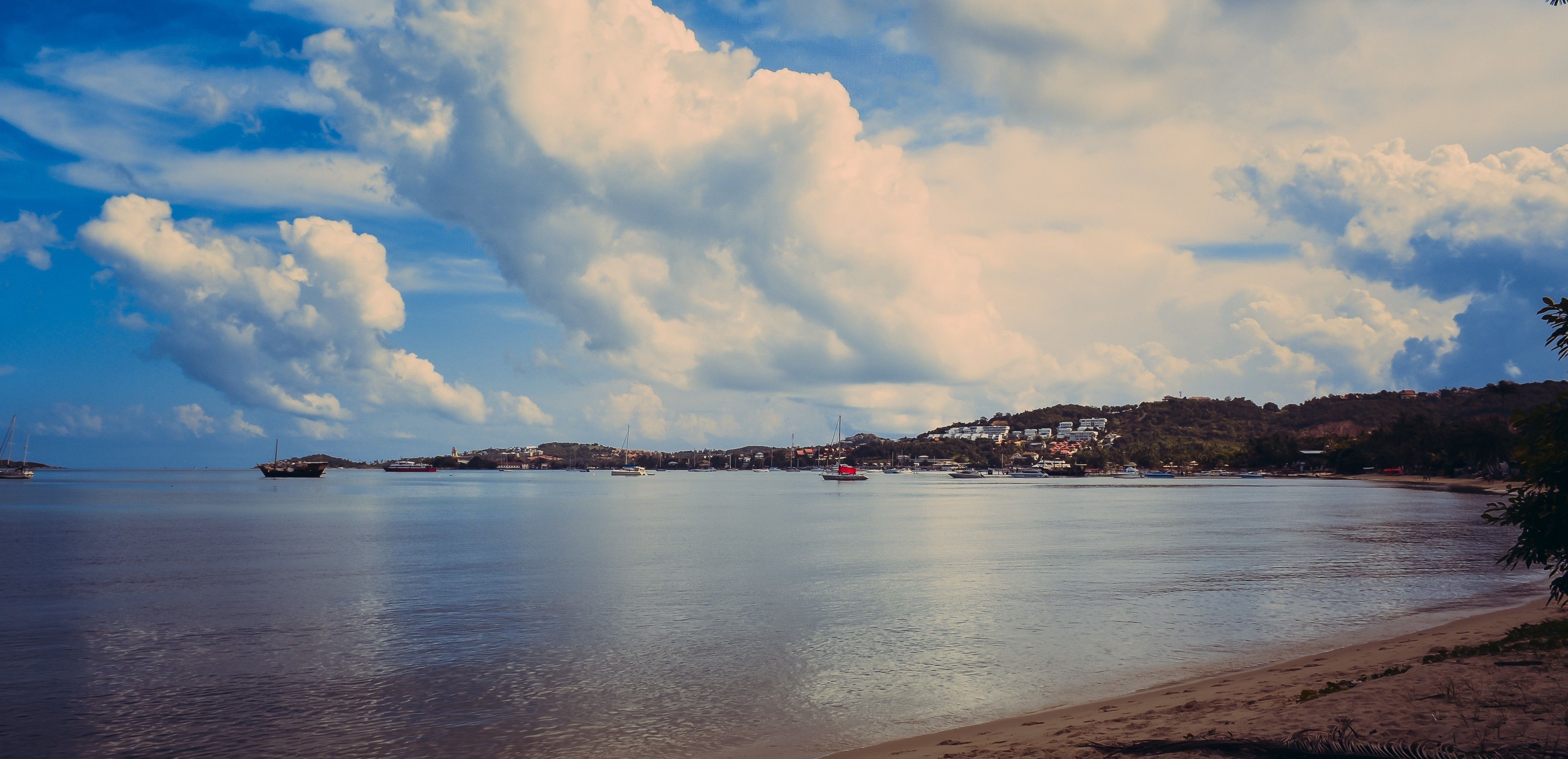 A coastal scene with a calm sea, boats, and a town on a hillside.