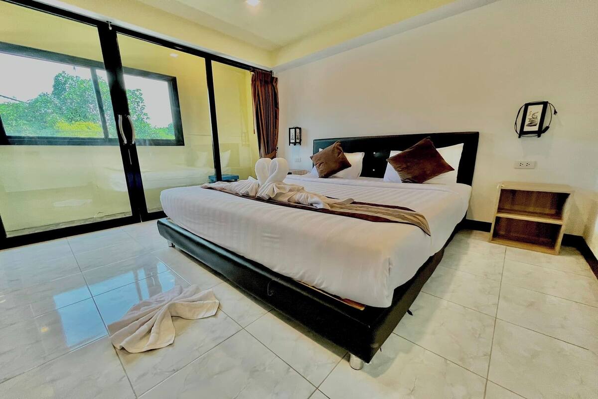 Habitación de hotel con una cama grande, una puerta corrediza de vidrio al exterior, una mesita de noche pequeña y una lámpara fijada a la pared.