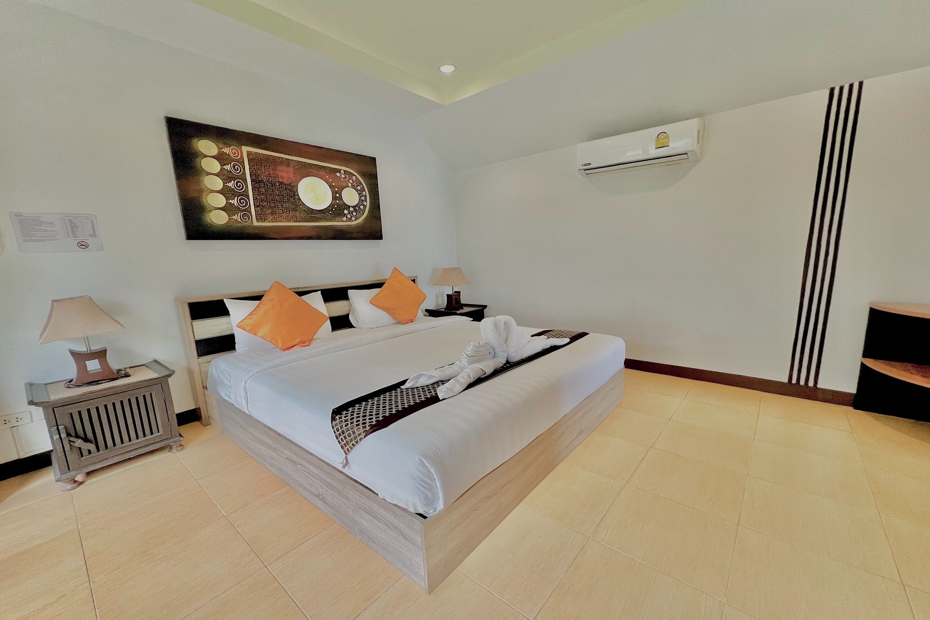 A hotel room with a bed, a nightstand, a lamp, a wall-mounted air conditioner, and a painting.