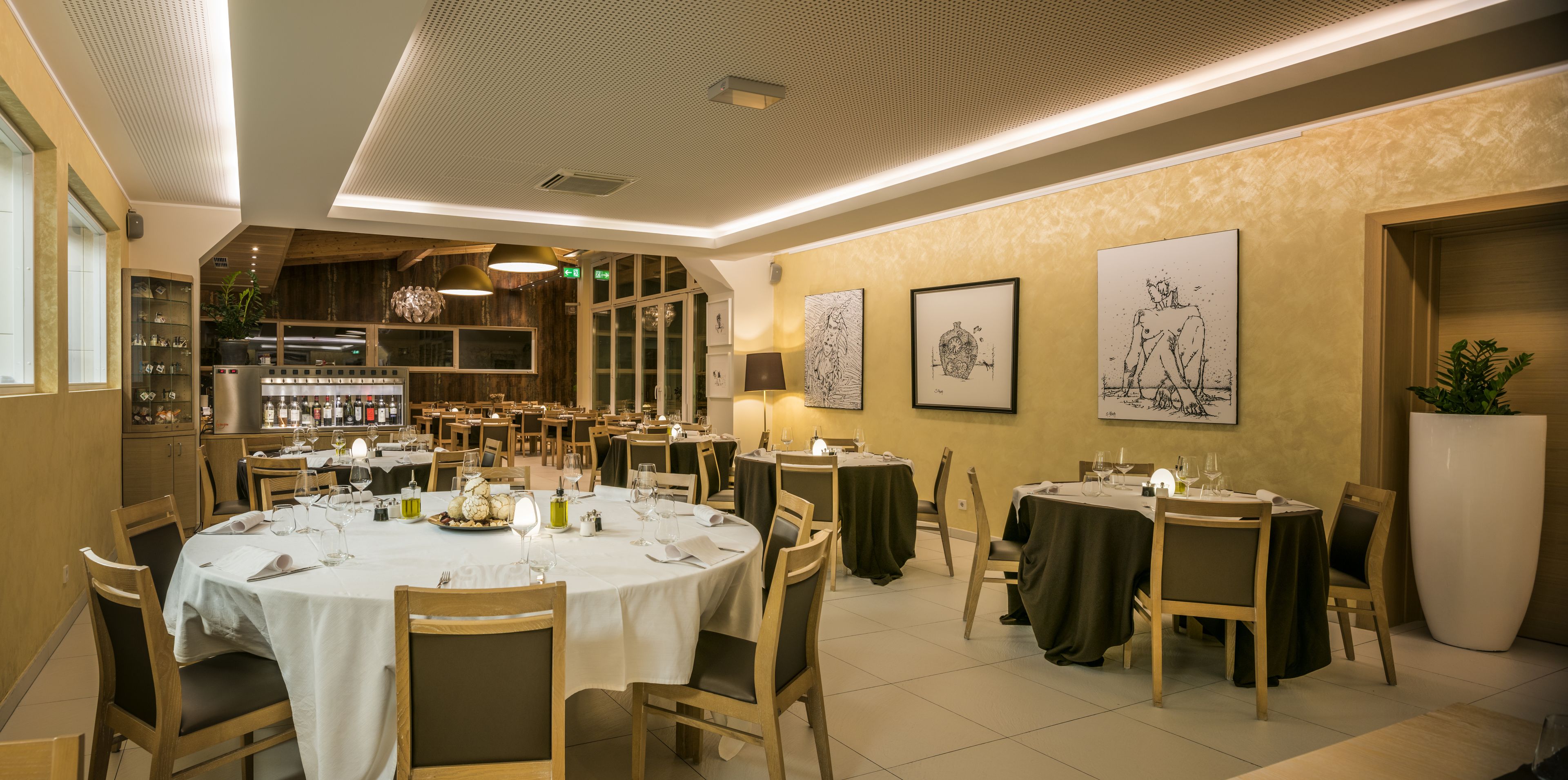 A restaurant with round tables, wooden chairs, and artwork on the walls.