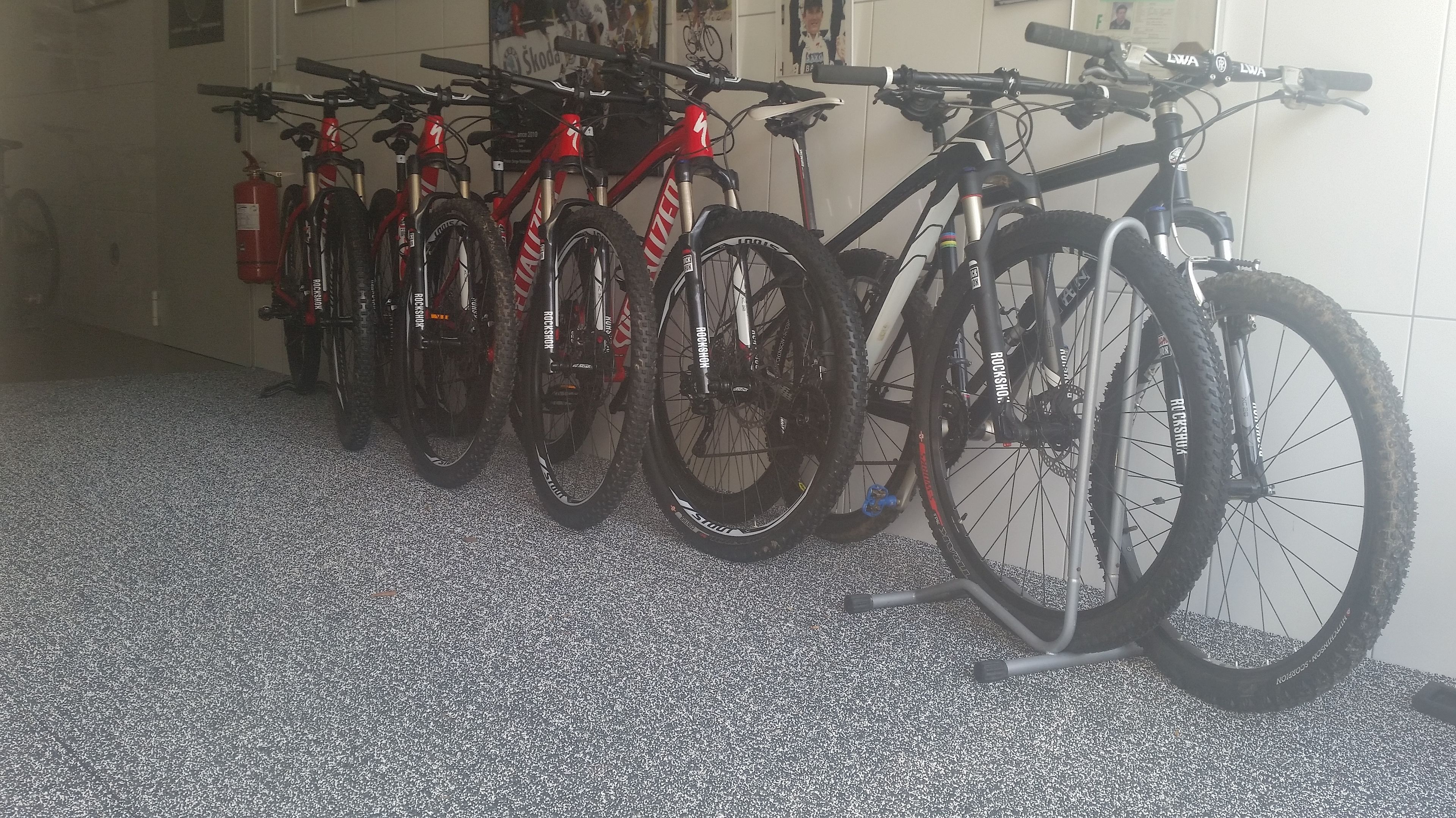 A row of bicycles parked indoors, with a fire extinguisher visible on the left.