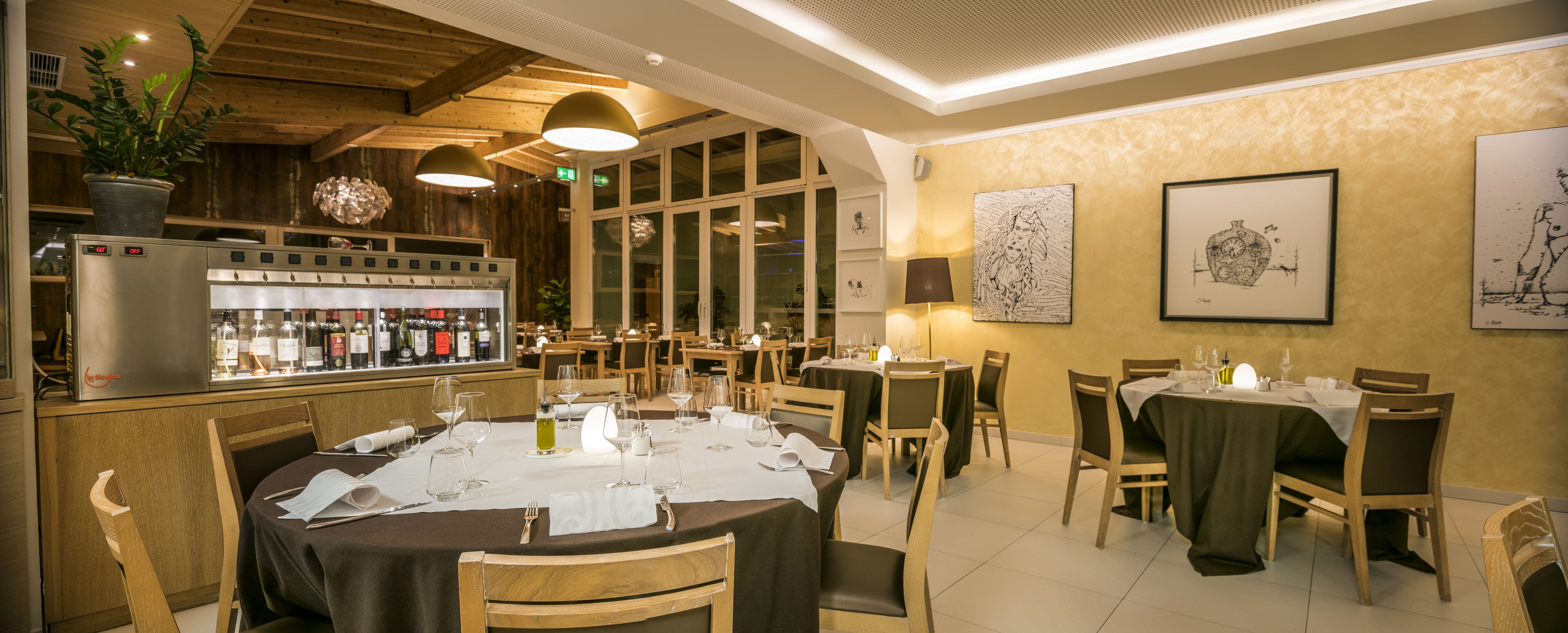 Um restaurante com decoração em madeira, área de bar com garrafas de vinho e obras de arte emolduradas nas paredes.