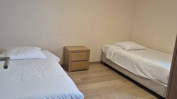 A small, clean room with two single beds, a wooden nightstand, and a light-colored wooden floor.
