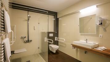 Un baño moderno con cabina de ducha de vidrio, inodoro blanco, lavabo con espejo y toallero.