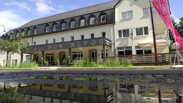 A hotel named "Hotel Bon Repos" with a modern design, featuring a large entrance and a visible reflection in the water in front. - Hotel Bon Repos (Consdorf)