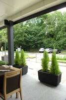 Un espacio al aire libre con mesas y sillas, plantas en macetas y vistas a coches estacionados y árboles.