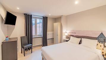 A hotel room with a bed, a desk, a chair, a TV, and a window with curtains.