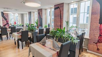 A modern restaurant interior with wooden flooring, black chairs, and tables set for dining.