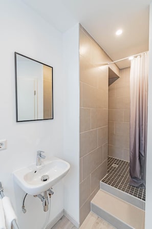 Un baño moderno con un lavamanos blanco, un espejo y una ducha con cortina.