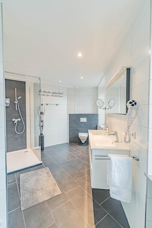 A modern bathroom with a shower, toilet, and two sinks.