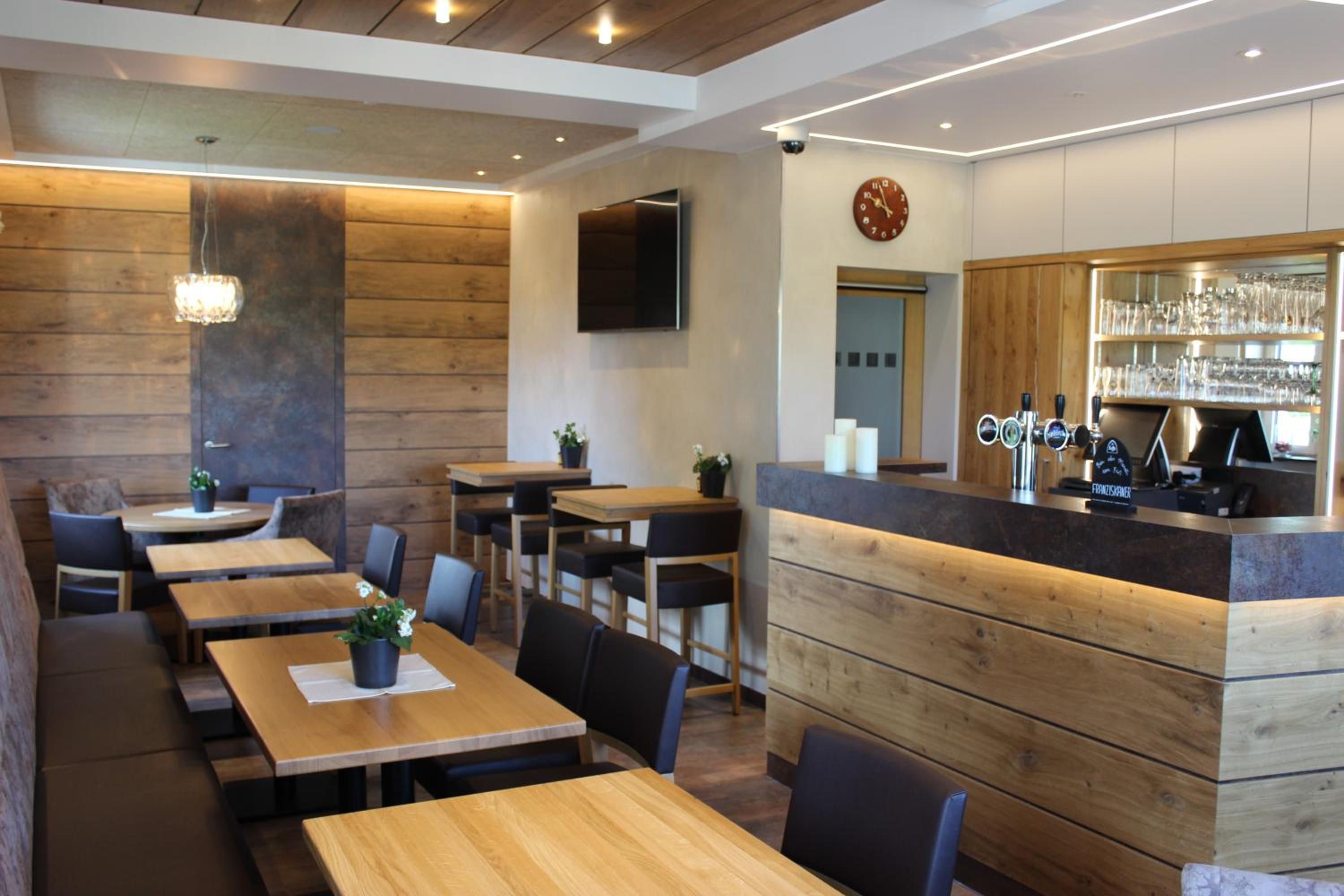 Ein Restaurantinneres mit Holztischen, Stühlen, einer Bar und einer Wanduhr.