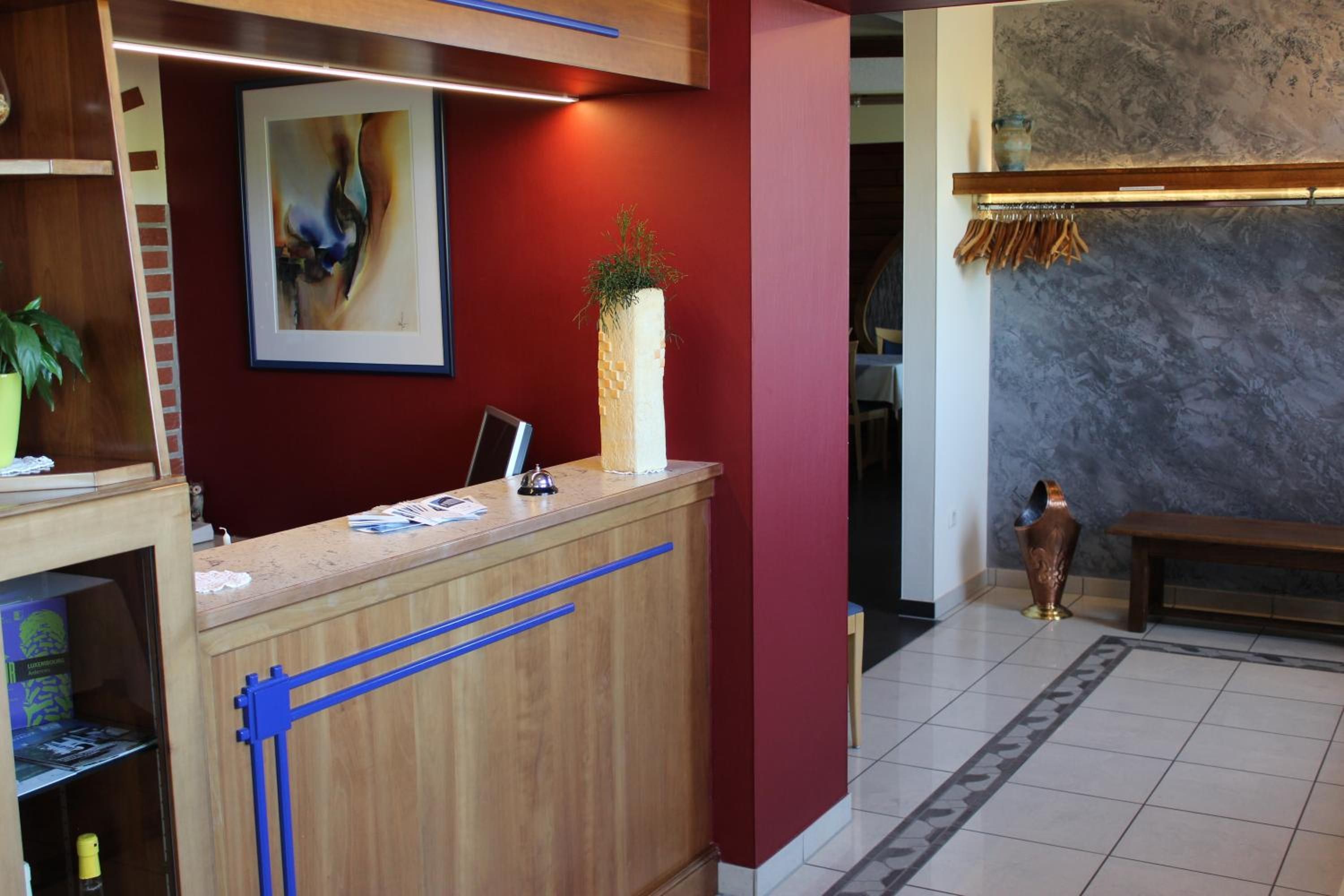 Ein Empfangstresen mit einem gerahmten abstrakten Gemälde, einer Topfpflanze und einer Bank in einer Lobby mit Fliesenboden und Marmorwand.