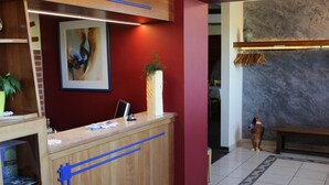 A reception desk with a framed abstract painting, a potted plant, and a bench in a lobby with a tiled floor and a marble wall.