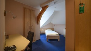 A hotel room with a desk, chair, bed, and a small bedside table.