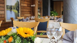 A restaurant interior with wooden walls, tables set with white tablecloths, chairs, and a centerpiece of sunflowers and flowers.