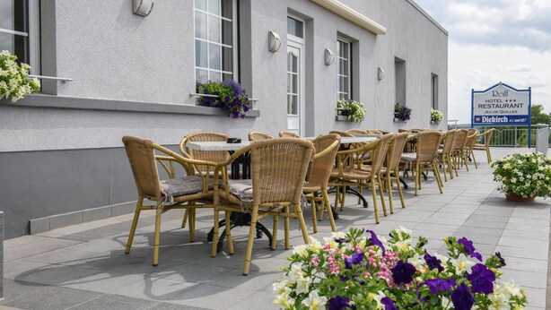 A row of wicker chairs and tables outside a building with a sign indicating a hotel and restaurant.