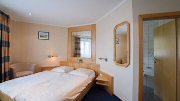 Een hotelkamer met een tweepersoonsbed, een stoel, een nachtkastje, een spiegel en een deur naar een badkamer.