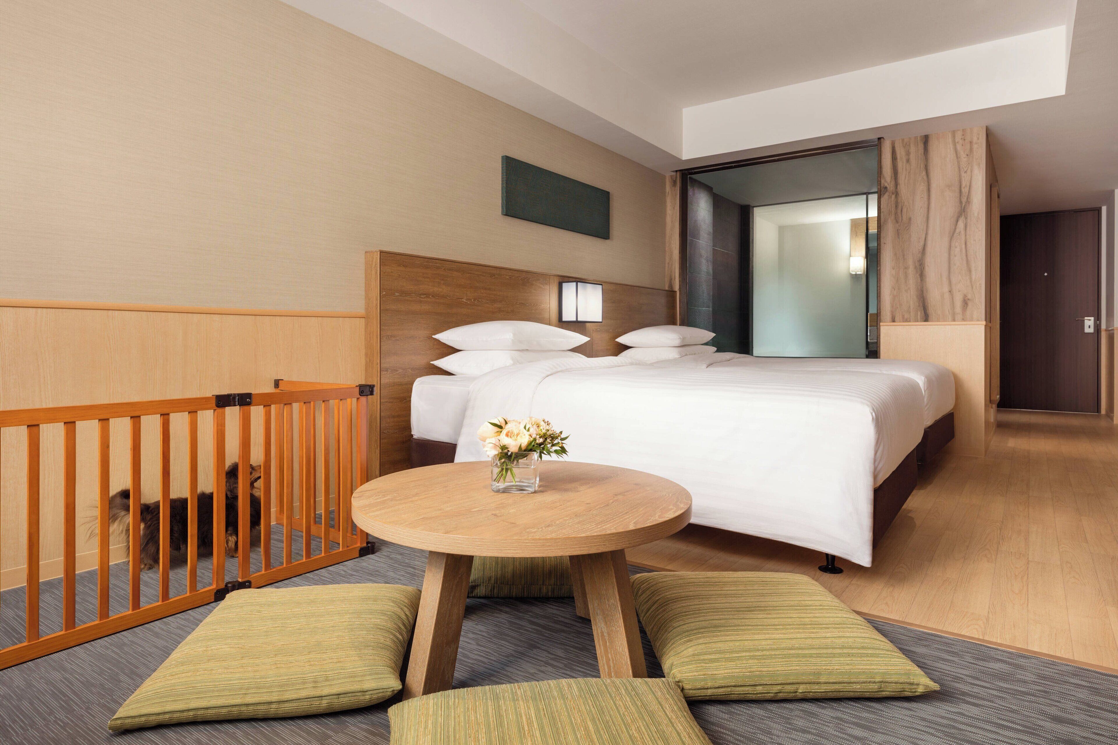 A hotel room with a bed, a round wooden table, and a pet-friendly area with a wooden fence.