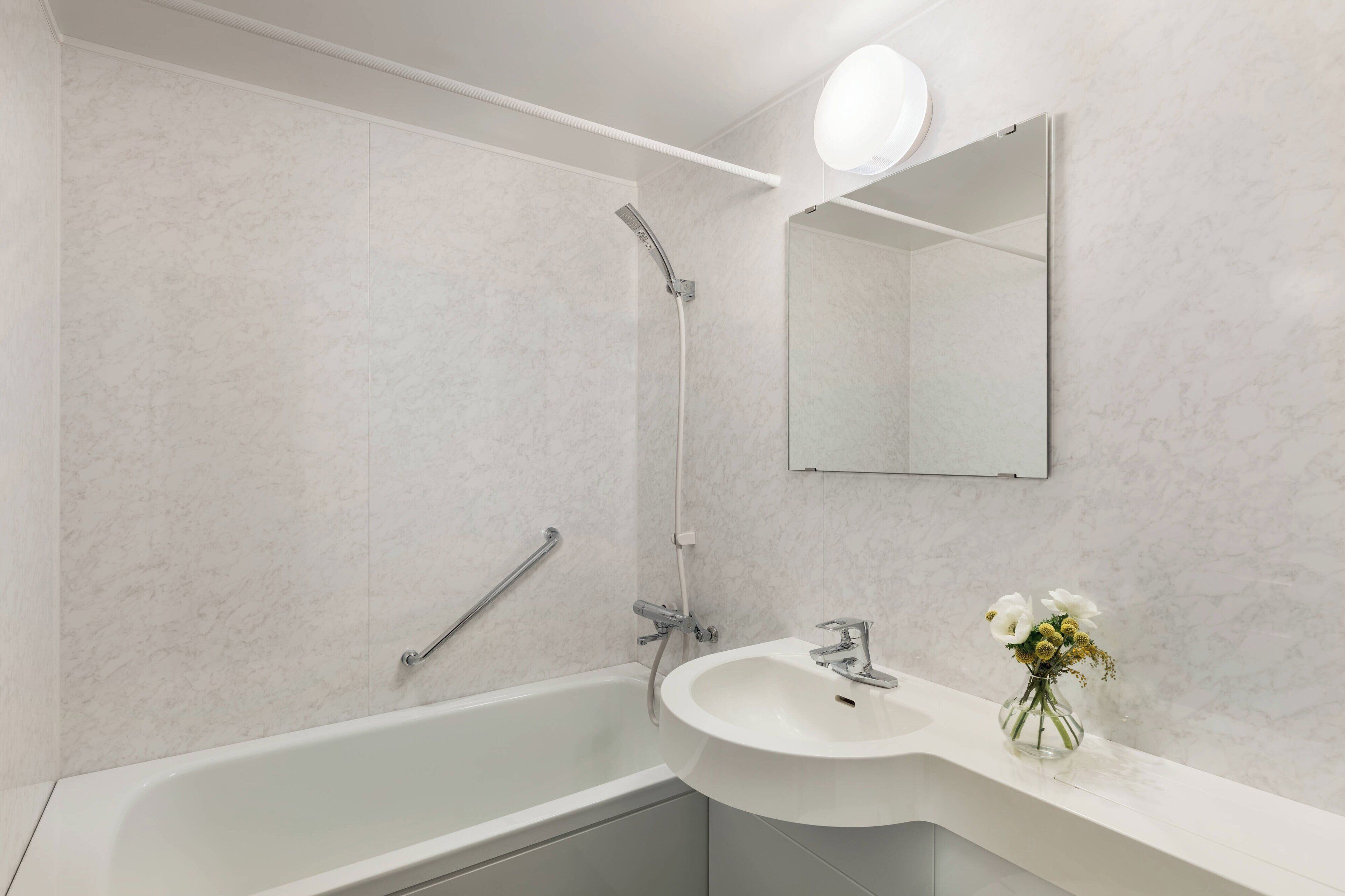 Une salle de bain moderne avec une baignoire blanche, un lavabo agrémenté d’un vase de fleurs et une douche.