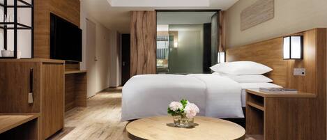 Una habitación de hotel moderna con una cama grande, muebles de madera, un televisor y una mesita con flores.