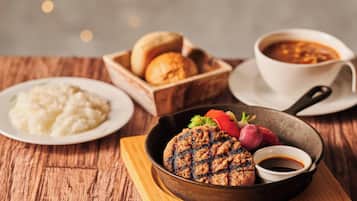 Un plato con carne a la parrilla, puré de papas y una taza de sopa sobre una mesa de madera.