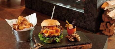 A burger with fries and mushrooms on a wooden board, with a fireplace in the background.