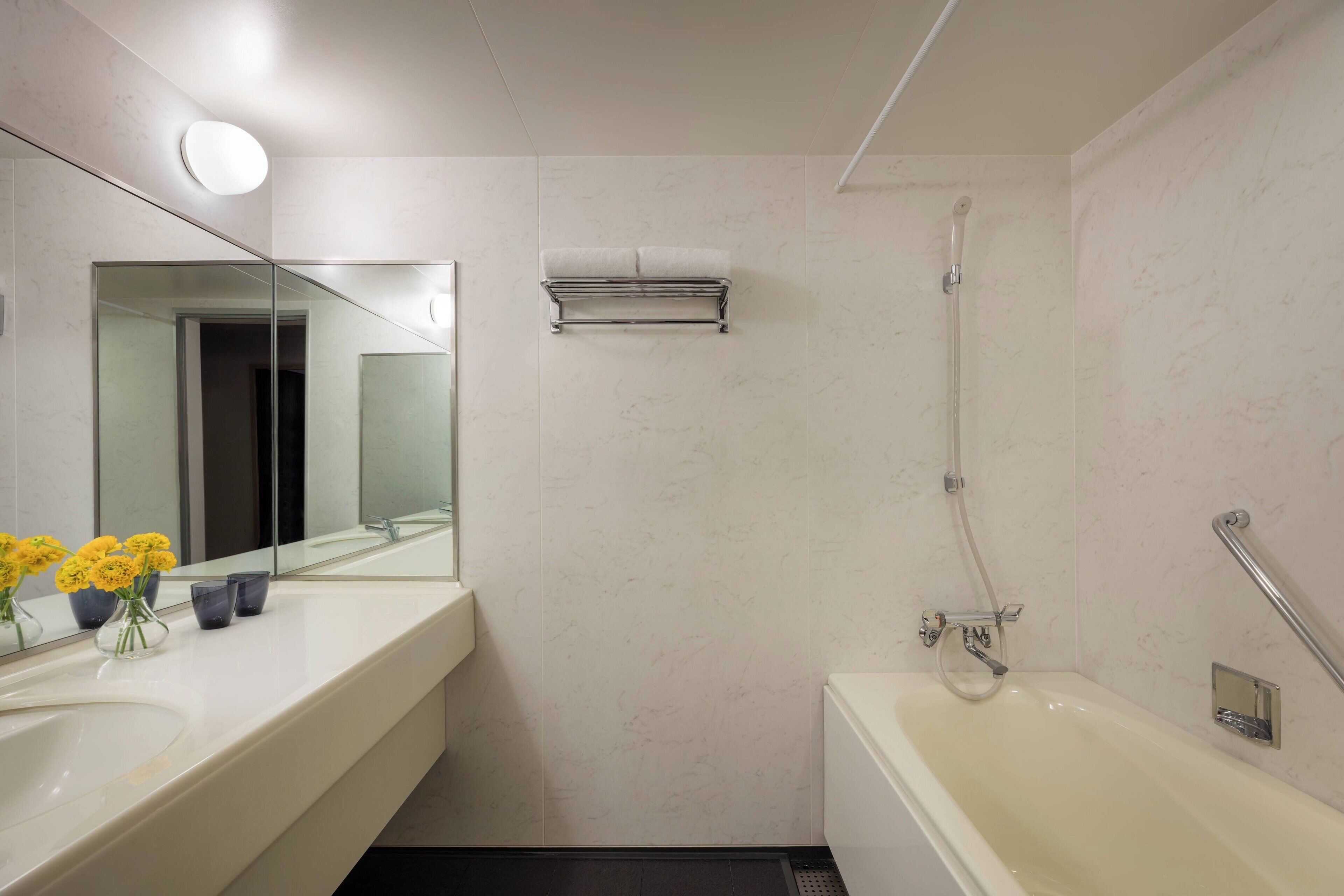 A modern bathroom with a large mirror, a white bathtub, and a shower.