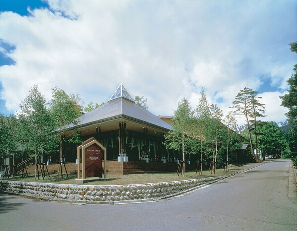 A building with a triangular roof, a stone wall in front, and trees around.