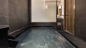A modern bathroom with a glass-enclosed hot tub, dark tiled walls, and a wooden shower enclosure.