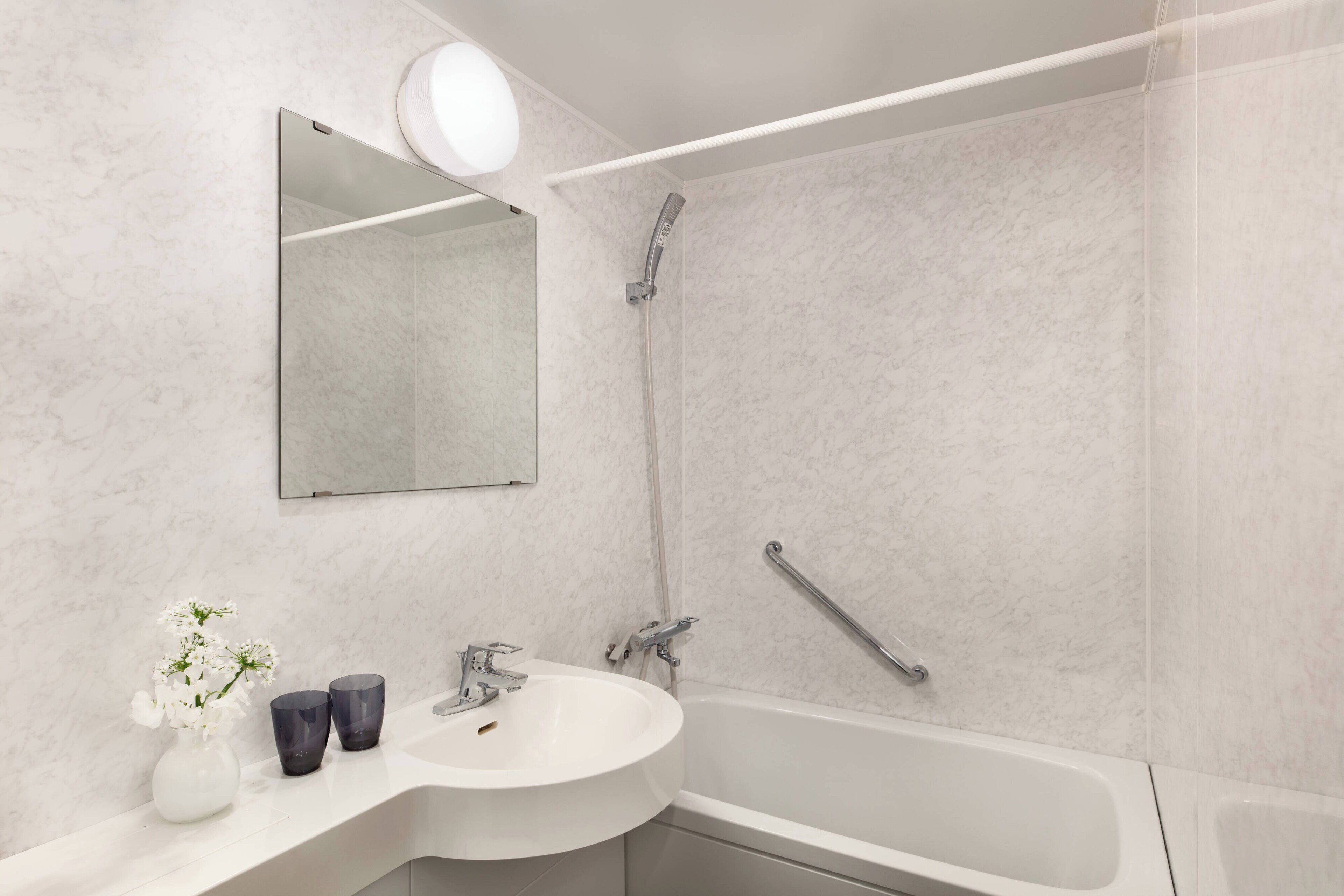 Un baño moderno con lavamanos, espejo y ducha blancos.