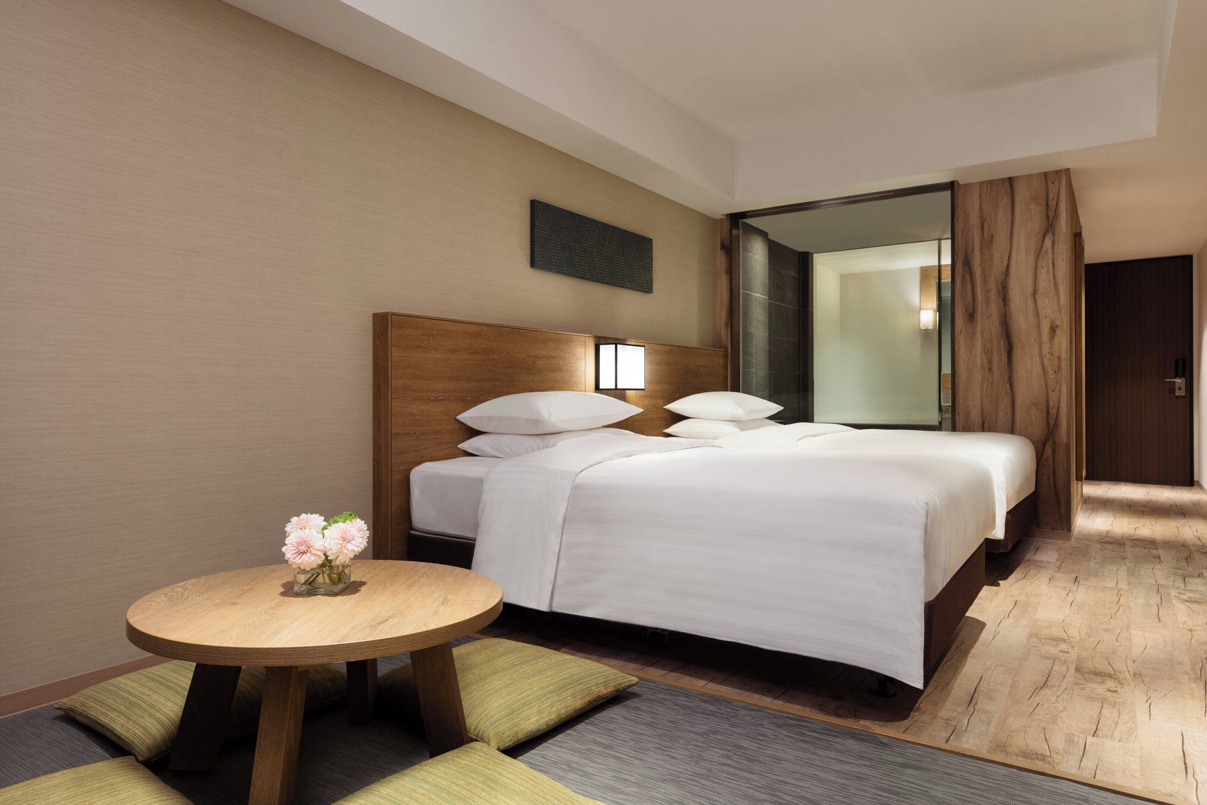 A hotel room with a large bed, a bedside table with a vase of flowers, and a small round table.