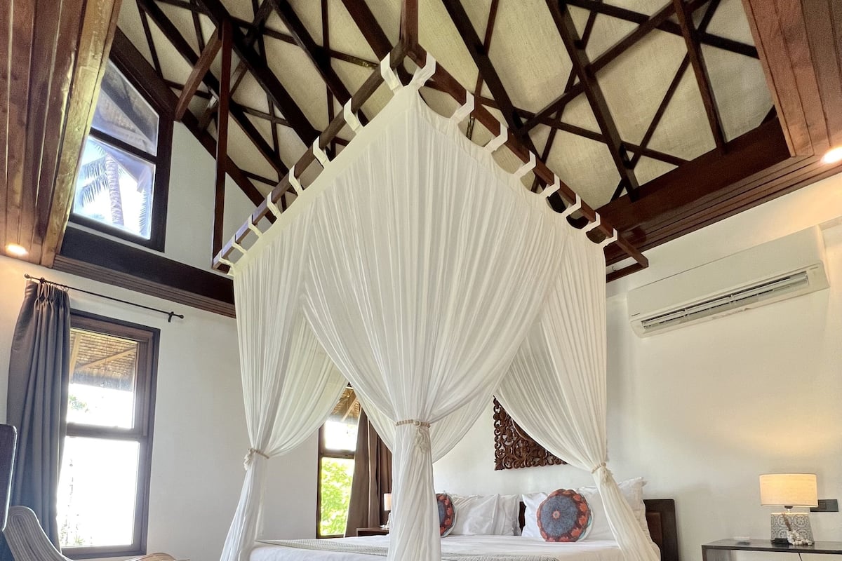 Un dormitorio con cama con dosel, suelo de madera y techo inclinado con vigas a la vista.