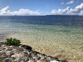 Vista despejada de una costa rocosa con aguas transparentes que conducen a una isla distante.
