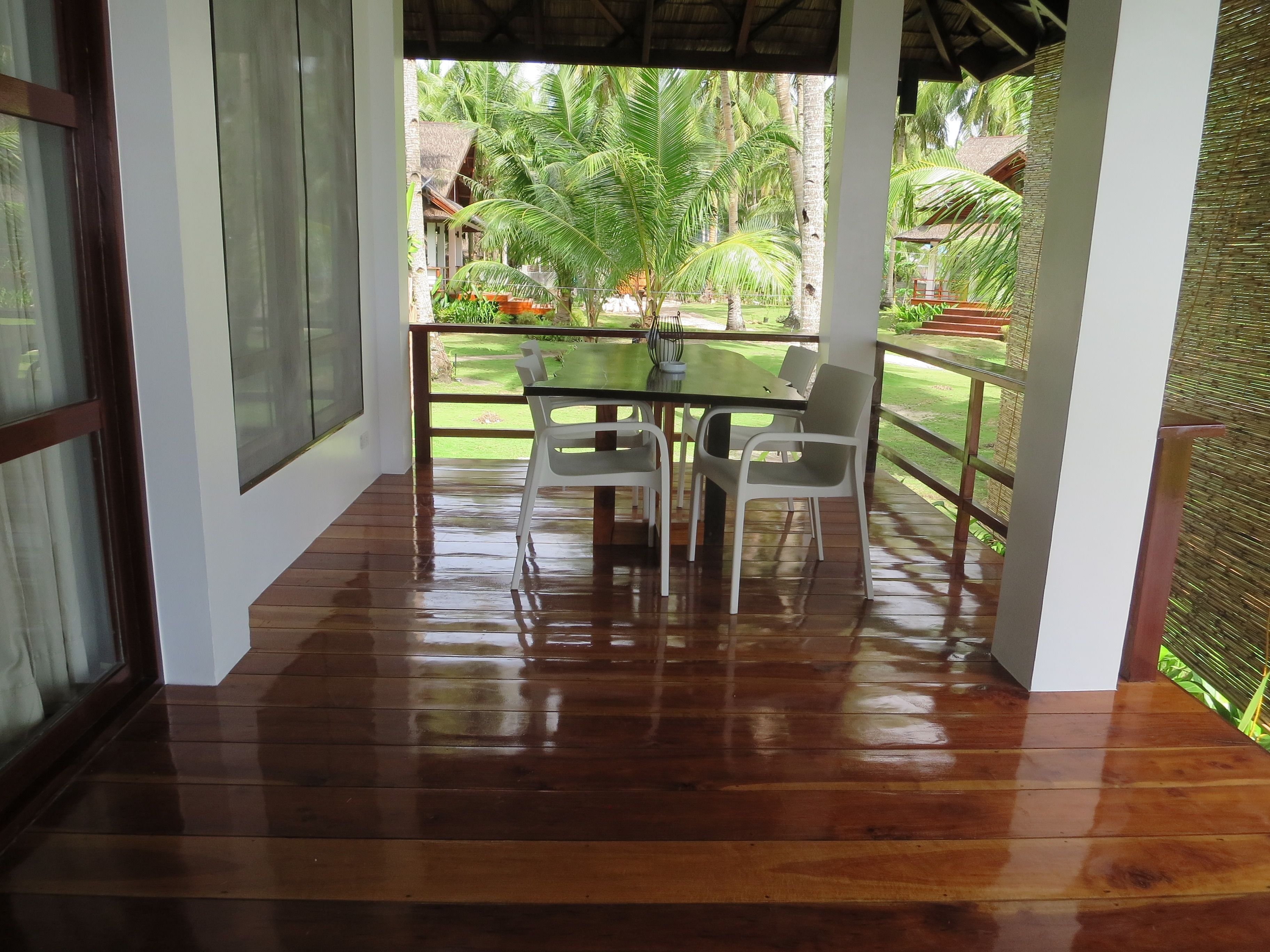 A wooden deck with a table and chairs, overlooking a garden with palm trees.